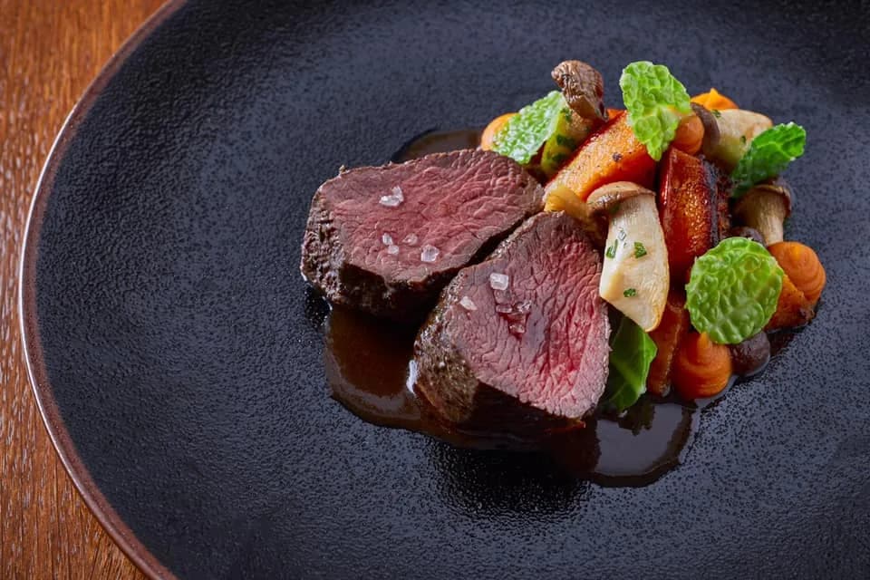 Steak z hovězí svíčkové s glazovanou kořenovou zeleninou a demi-glace na černém talíři